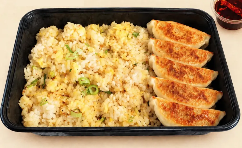 Stekta gyoza bredvid stekt ris med ägg och salladslök i en svart låda, med en kopp chiliolja